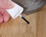Mit einem Lackstift und Schleifpapier werden Kratzer auf dem Laminat repariert.
