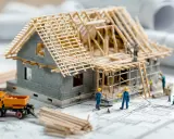 Modellhaus im Rohbau mit kleinen Arbeitern, Bauplänen und einem Bagger. Einblick in die **Kosten Neubau**.