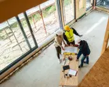 Bauarbeiter und Architektin besprechen Pläne für den Ausbauhaus Kosten. Sie stehen an einem Tisch mit Werkzeugen und Farbpaletten.
