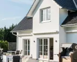 Modernes Haus mit weißen Wänden, dunklem Dach und großer Terrasse. Verschiedene haus stile sind hier vereint, von der Fassade bis zur Gartengestaltung.