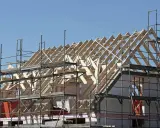 Holzkonstruktion eines Dachstuhls im Bau, umgeben von Gerüsten. Ein Architekt plant den Bau dieses Hauses.