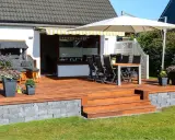 Eine schöne garten terrasse mit Holzdielen, Sitzmöbeln, Sonnenschirm und Blumen. Perfekt für entspannte Stunden im Freien.
