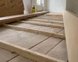 Holzbalken werden auf alten Dielen verlegt, um den Untergrund für einen neuen Dielenboden auszugleichen.