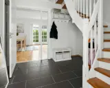 Helle Diele mit dunklem Fliesenboden, Spiegel, Garderobe und einer weißen Treppe, die auf eine **steintreppe renovieren**-Idee hindeutet.