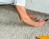 Handwerker verlegt Teppich mit einem Cuttermesser und einem Zollstock.