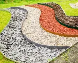 Geschwungene Beete mit verschiedenen Schichten aus grauem Schiefer, hellem Kies, roter Rindenmulch und dunklem Rindenmulch, die durch Metallkanten für rasenkanten setzen getrennt sind.