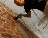 Mann mit Handschuhen trägt eine Masse auf eine Ziegelwand auf, um Anschlussfugen abzudichten.