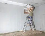 Mann auf Leiter montiert weiße Platten zur kellerdecke isolieren.