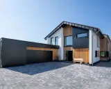 Modernes Haus mit Garage, dessen Satteldach modern interpretiert ist. Holz und dunkle Fassadenelemente prägen das Bild.