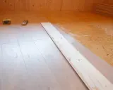 Holzboden wird verlegt. OSB-Platten sind mit Kleber vorbereitet, darauf werden helle Dielen verlegt.