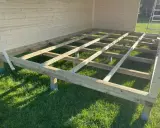 Holzkonstruktion für das Gartenhaus. Der Boden wird auf Balken und Pfosten errichtet, die auf dem Rasen stehen.