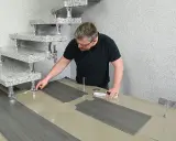 Mann verlegt PVC-Boden. Die grauen Planken werden passgenau zugeschnitten und neben einer modernen Treppe ausgelegt.
