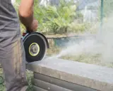 Mann schneidet mit Winkelschleifer Terrassenplatten. Staub wirbelt auf.