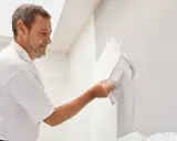 Mann verputzt eine Wand mit einer Kelle. Die Arbeit im Bad ist fast fertig.