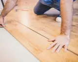 Mann verlegt Laminat. Die Holzoptik der Dielen wird sorgfältig zusammengefügt.