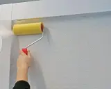 Mit einem gelben Farbroller wird eine weiße Tapete spachteln.