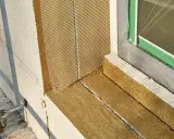 Fensterlaibung wird mit Steinwolle gedämmt. Das Material wird sorgfältig zugeschnitten und mit Armierungsgewebe versehen, um es vor dem Kleben vorzubereiten.