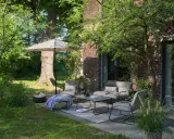 Gemütliche kleine Terrasse gestalten mit bequemen Sitzmöbeln, Tisch, Sonnenschirm und Kissen. Einladend und grün.