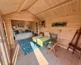 Gemütlicher Gartenhaus Innenausbau mit Tagesbett, Esstisch und Staffelei. Holzwände und Decke schaffen eine warme Atmosphäre.