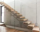 Moderne Holztreppe mit Glasgeländer an Betonwand. Hier können Sie die treppe kosten berechnen.