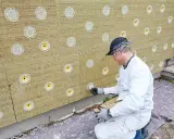 Mann befestigt Tellerdübel in Mineralwolle-Dämmplatten für eine Fassadenisolierung.