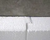 Styroporplatten werden zugeschnitten, um ein Kellerfenster zu isolieren. Die weißen Platten sind aneinandergefügt und grenzen an eine graue Betonfläche.