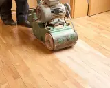 Ein Handwerker bearbeitet mit einer Schleifmaschine einen Holzboden. Das Parkett wird abgeschliffen, um ihm neues Leben einzuhauchen.