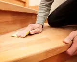 Mann schleift mit Sandpapier eine Holztreppe, um sie zu renovieren.