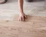 Hände legen Holzplanken auf Kleber, um den Boden zu verlegen.