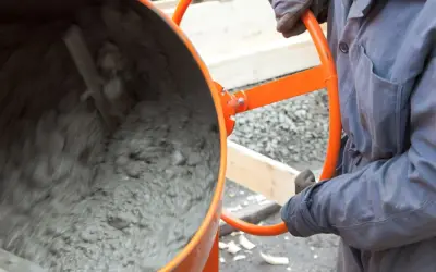 Person in Arbeitskleidung bedient eine Betonmischmaschine, um Beton zu mischen.
