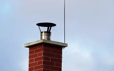 Ein roter Ziegelkamin mit einem Blitzableiter, der über dem Schornstein auf einem Haus thront, schützt vor Gewittern.