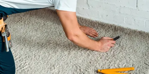 Handwerker verlegt Teppich mit einem Cuttermesser und einem Zollstock.