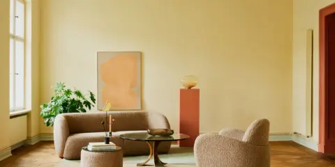 Ein Wohnzimmer mit gelben Wänden und einem frisch gestrichenen, hellgrünen Decke. Gemütliche Bouclé-Möbel und ein moderner Couchtisch laden zum Verweilen ein.