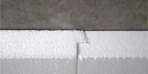 Styroporplatten werden zugeschnitten, um ein Kellerfenster zu isolieren. Die weißen Platten sind aneinandergefügt und grenzen an eine graue Betonfläche.