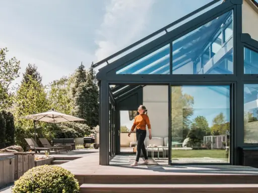 Frau betritt modernen Wintergarten mit Glasdach. Perfekt, um den Sommer zu verlängern und den **Wintergarten planen**.