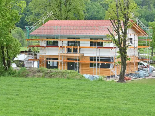 Ein Haus im Bau, umgeben von Gerüsten. Man sieht, wie man ein Haus baut, mit Holzfassade und rotem Ziegeldach.