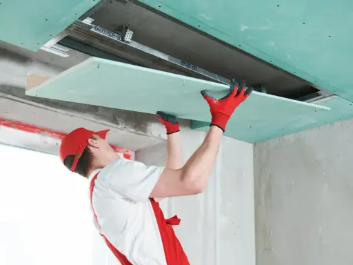 Handwerker mit roten Handschuhen montiert Gipskartonplatten an der Decke, um das Zimmer zu isolieren.