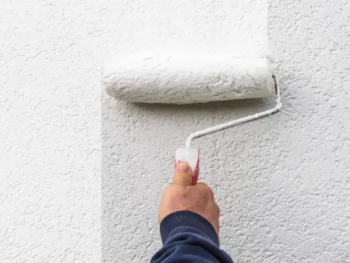 Hand rollt weiße Farbe auf eine strukturierte Wand. Man sieht, welche Wandfarbe am besten deckt.
