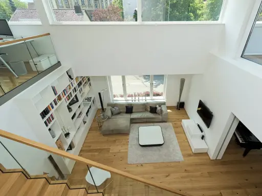 Ein offener Wohnbereich mit viel Licht und Raum. Die moderne luftraum architektur mit großen Fenstern und einer offenen Treppe schafft ein Gefühl von Weite.