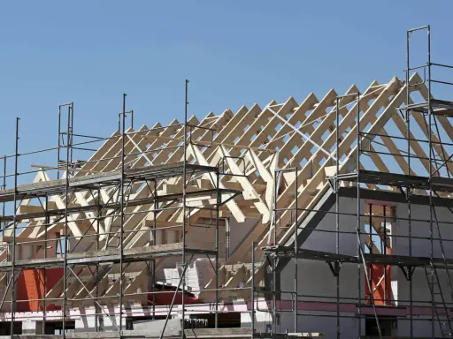 Holzkonstruktion eines Dachstuhls im Bau, umgeben von Gerüsten. Ein Architekt plant den Bau dieses Hauses.