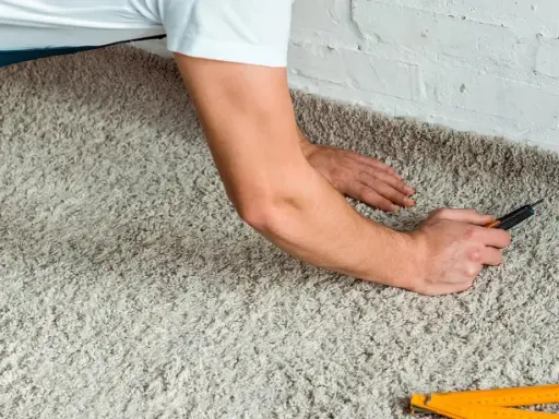 Handwerker verlegt Teppich mit einem Cuttermesser und einem Zollstock.