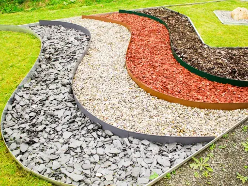 Geschwungene Beete mit verschiedenen Schichten aus grauem Schiefer, hellem Kies, roter Rindenmulch und dunklem Rindenmulch, die durch Metallkanten für rasenkanten setzen getrennt sind.