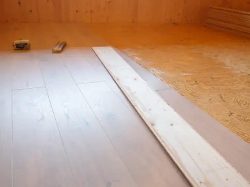 Holzboden wird verlegt. OSB-Platten sind mit Kleber vorbereitet, darauf werden helle Dielen verlegt.