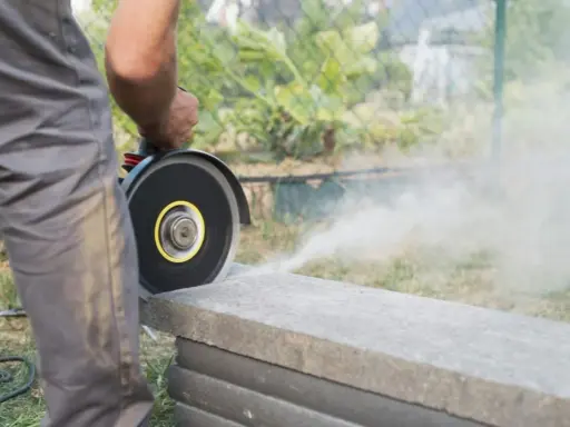 Mann schneidet mit Winkelschleifer Terrassenplatten. Staub wirbelt auf.