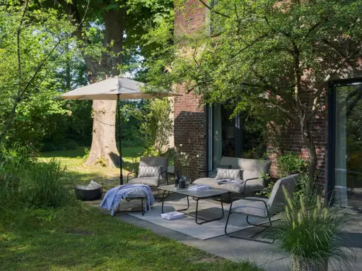 Gemütliche kleine Terrasse gestalten mit bequemen Sitzmöbeln, Tisch, Sonnenschirm und Kissen. Einladend und grün.