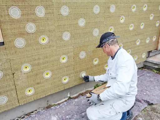 Mann befestigt Tellerdübel in Mineralwolle-Dämmplatten für eine Fassadenisolierung.