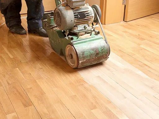 Ein Handwerker bearbeitet mit einer Schleifmaschine einen Holzboden. Das Parkett wird abgeschliffen, um ihm neues Leben einzuhauchen.