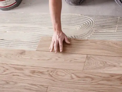Hände legen Holzplanken auf Kleber, um den Boden zu verlegen.