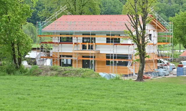 Ein Haus im Bau, umgeben von Gerüsten. Man sieht, wie man ein Haus baut, mit Holzfassade und rotem Ziegeldach.