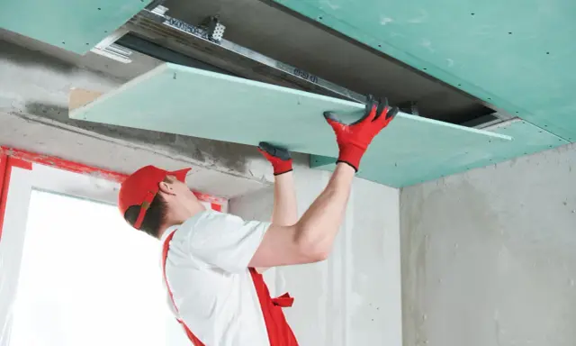 Handwerker mit roten Handschuhen montiert Gipskartonplatten an der Decke, um das Zimmer zu isolieren.